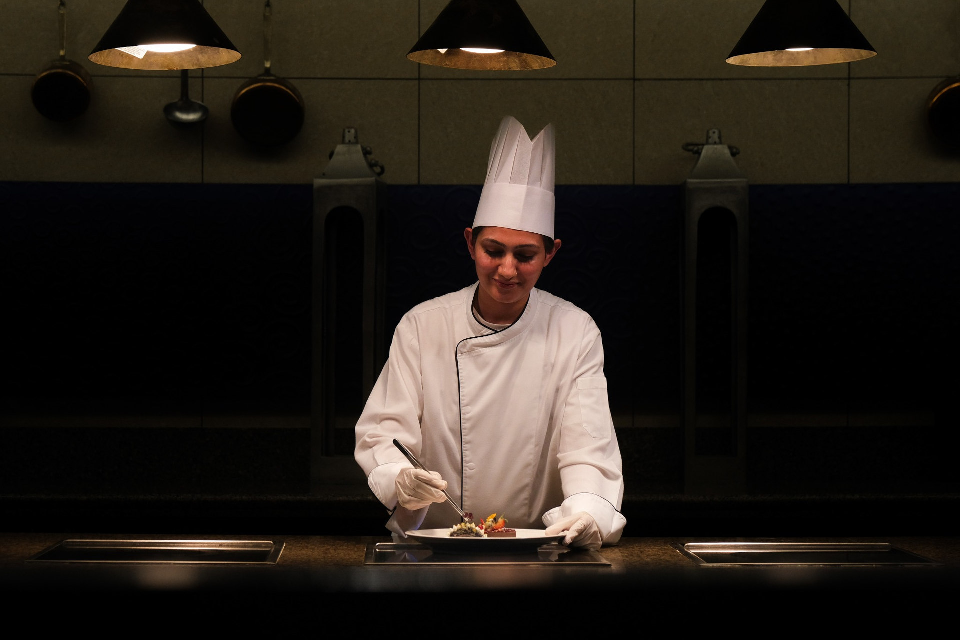 Chef garnishing dish in dark kitchen