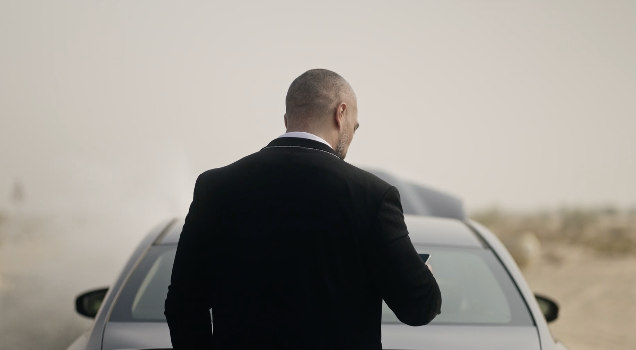 Suited figure beside car in pale desert setting